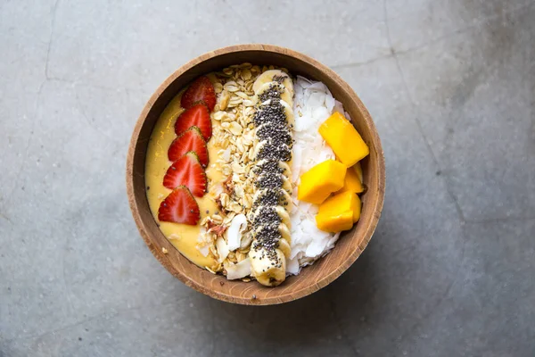 芒果冰沙碗与草莓 椰子和燕麦片的混凝土背景 健康食品概念 顶部视图 图库图片
