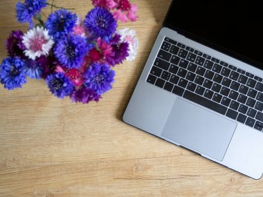 Dizüstü bilgisayarlı ve çiçekli işyeri manzarası.