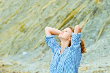 Deniz kıyısında mavi çizgili gömlek ve kot şortlu genç bir kadın.
