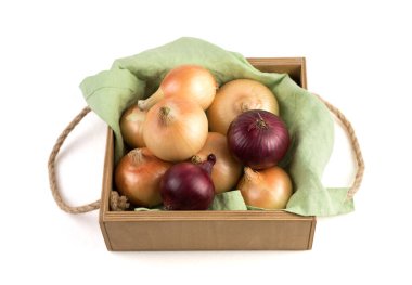 Beyaz bir arka planda izole edilmiş keten peçeteye sarılı ahşap bir kutuda farklı çeşitteki soğanlar..