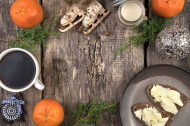 Konforlu bir Noel kompozisyonu, kozalaklı dallar, mandalinalar, bir fincan kahve ve sandviç, bir not defteri ve doğal ahşap arka planda bir retro kamera..