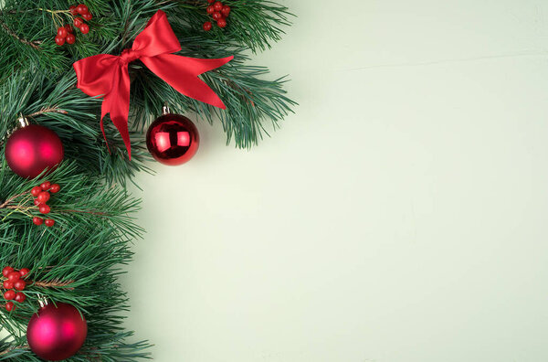 Decorated with red Christmas toys, bows and glass balls, pine branches on a light green background.