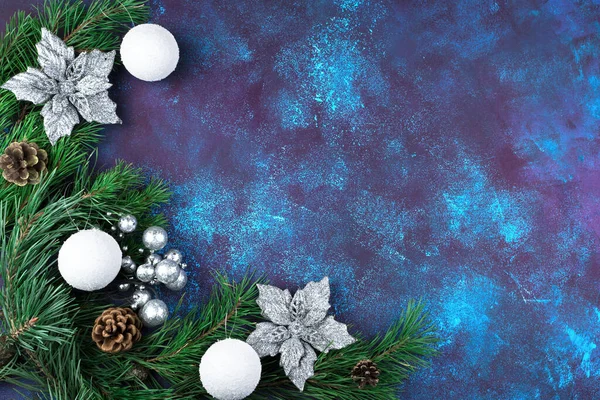 Зелені гілки сосни прикрашені красивими срібними квітами, шишками та новорічними іграшками на синьому бетонному фоні . — стокове фото