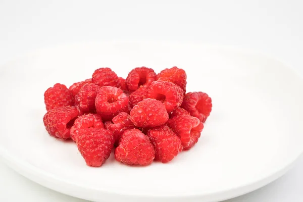 Frambuesas frescas en pequeñas cantidades se colocan en un plato blanco sobre un fondo claro. —  Fotos de Stock