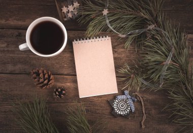Not defteri, kahve fincanı ve tahtadan bir arka planda Noel süslemeleri..
