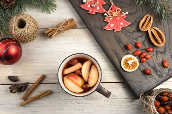 Warm Christmas drink on a wooden Board surrounded by berries, cinnamon sticks, fir branches and toys on a wooden background. — Stock Photo, Image