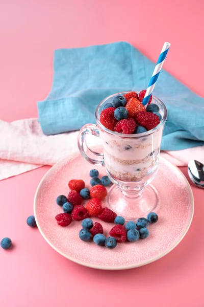 Cream with berries and muesli in a transparent glass on a soft pink background. — Stock Photo, Image