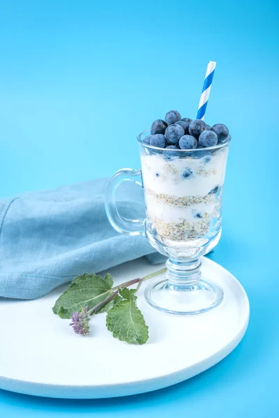 Berries, nuts, cream in a clear glass on a soft blue background.