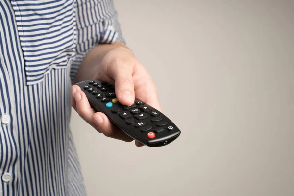 Remote control in the hands of a woman on a beige background.