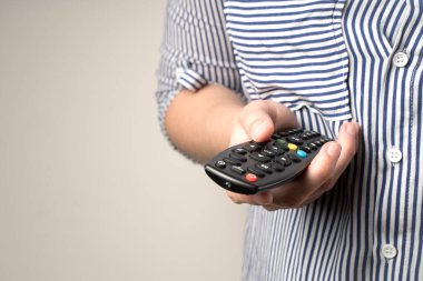 Bir kadın bej arka planda uzaktan kumanda tutuyor..