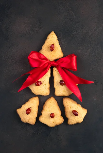 The cookies are laid out in the shape of a Christmas tree with a red bow on a brown concrete background. — Stock Photo, Image