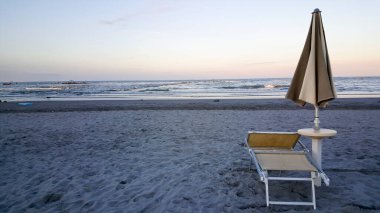 Şafak vakti rimini üzerinde güneş rumbrellaları ve şafak vakti rimini 'nin rimini' sinde güneş sularından yansıyan iskemlelerle şemsiyeler ve şezlonglar kapanıyor. Yüksek kalite fotoğraf