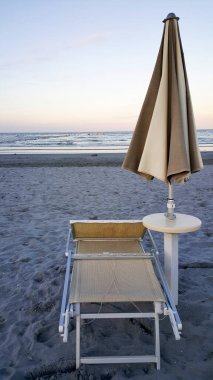 Şafak vakti rimini üzerinde güneş rumbrellaları ve şafak vakti rimini 'nin rimini' sinde güneş sularından yansıyan iskemlelerle şemsiyeler ve şezlonglar kapanıyor. Yüksek kalite fotoğraf