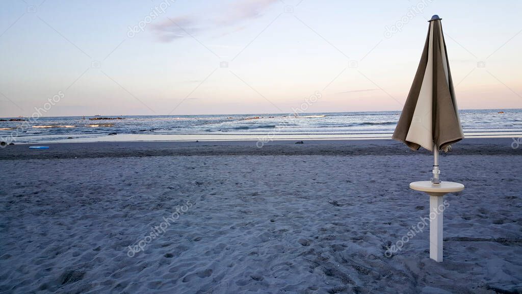 umbrellas and deckchairs closed at dawn on the rimini of rimini with sun rumbrellas and deckchairs closed at dawn on the rimini of rimini with sun reflecting off the wateeflecting off the wate. High quality photo