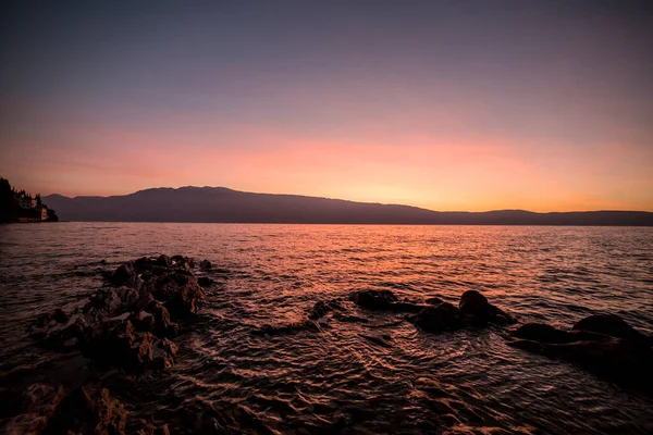 ガルダ湖の美しい日の出は太陽の色を反映して岩や波と共に上がりました — ストック写真