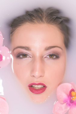 Fotoğraflar için süt ve çiçek dolu bir küvette poz veren güzel bir kız.