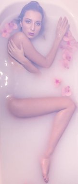 Fotoğraflar için süt ve çiçek dolu bir küvette poz veren güzel bir kız.