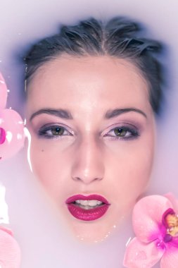 Fotoğraflar için süt ve çiçek dolu bir küvette poz veren güzel bir kız.