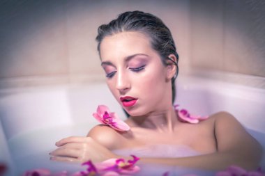 Fotoğraflar için süt ve çiçek dolu bir küvette poz veren güzel bir kız.