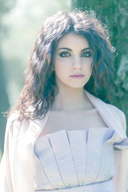 Uzun saçlı güzel esmer kız yeşil parkta uzun pembe elbiseli poz veriyor. Yüksek kalite fotoğraf