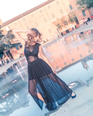 Suyun ortasında dans eden güzel sarışın kız Reggio Emilia çeşmesinde uzun şeffaf elbisesiyle