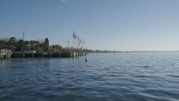シルミオーネの桟橋とガルダ湖の岸に美しい晴れた日に旗とポート — ストック動画