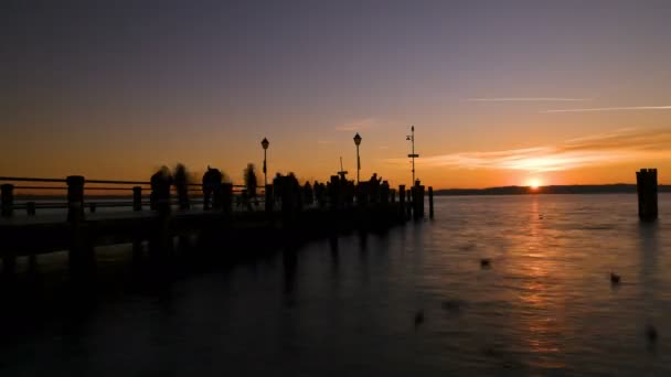 日落时与人在加尔达湖上美丽的时光飞逝码头 — 图库视频影像