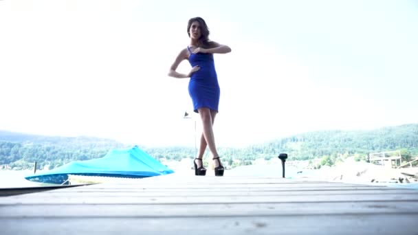 美丽的黑发女孩，长发，身穿蓝色性感短裙，脚后跟，站在码头上 — 图库视频影像