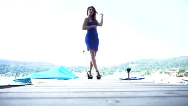 schöne brünette Mädchen mit langen Haaren posiert auf barce Pier mit blauem sexy kurzes Kleid und Fersen