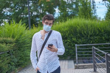 beautiful young man walking around the city with anti covid 19 surgical mask. High quality photo clipart