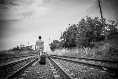 Delikanlı trenin raylarında trolly bavuluyla yürüyor. Yüksek kalite fotoğraf