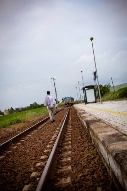 Genç adam tren raylarında ceket ve şapkayla yürüyor. Yüksek kalite fotoğraf