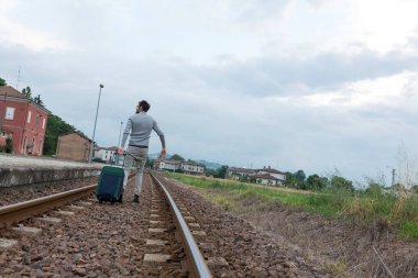 Delikanlı trenin raylarında trolly bavuluyla yürüyor. Yüksek kalite fotoğraf