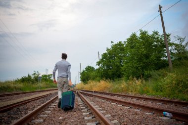 Delikanlı trenin raylarında trolly bavuluyla yürüyor. Yüksek kalite fotoğraf