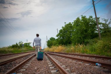 Delikanlı trenin raylarında trolly bavuluyla yürüyor. Yüksek kalite fotoğraf