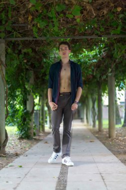 Güzel çocuk, açık gömlekli ve vücutlu bir pergola yaprakları arasında poz veriyor. Yüksek kalite fotoğraf