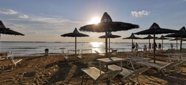 Güneşin doğuşu, açık şemsiyeli Cesenatio Riccione Rimini plajını yansıtıyor. Yüksek kalite fotoğraf
