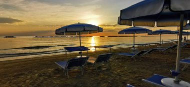 Güneşin doğuşu, açık şemsiyeli Cesenatio Riccione Rimini plajını yansıtıyor. Yüksek kalite fotoğraf