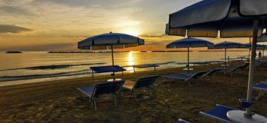 beautiful sunrise with sun reflection on cesenatio riccione rimini beach with open umbrellas. High quality photo clipart