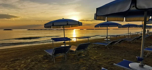 Güneşin doğuşu, açık şemsiyeli Cesenatio Riccione Rimini plajını yansıtıyor. Yüksek kalite fotoğraf