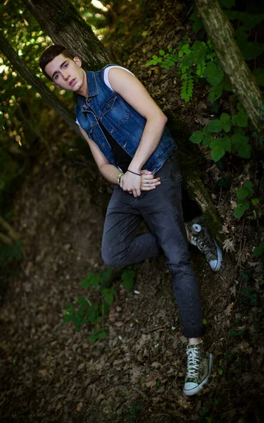 森の中でジーンジャケットを着て屋外でポーズをとる美しい男 — ストック写真