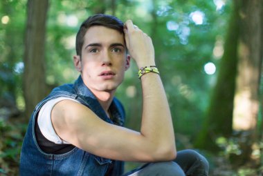 Güzel bir adam ormanda kot ceketle poz veriyor.