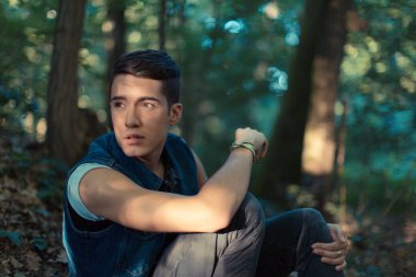 Güzel bir adam ormanda kot ceketle poz veriyor.
