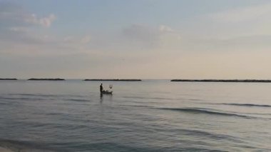 Güneş batarken sakin Adriyatik Denizi 'nde kürek çeken bir insanın huzurlu ve manzaralı görüntüsü suya güzel bir altın yansıma yansıtıyor. Riviera Romagnola Cesenatico Rini 'de. Yüksek kalite