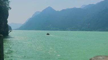 Küçük bir motorlu tekne, heybetli dağlarla çevrili sakin bir alp gölünün turkuaz yeşili sularında yol alır. Ledro Gölü. Yüksek kalite 4k görüntü