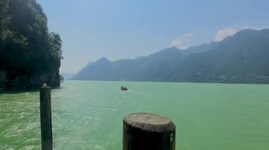 Küçük bir motorlu tekne, heybetli dağlarla çevrili sakin bir alp gölünün turkuaz yeşili sularında yol alır. Ledro Gölü. Yüksek kalite 4k görüntü