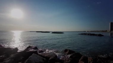 Sabah güneşi, İtalya 'nın Cesenatico kentindeki sakin Adriyatik Denizi üzerinde yükseliyor. Işık, güzel bir yaz sabahında kayalık bir dalgakırandan görülen sakin suyu yansıtır. Yüksek kalite 4k görüntü