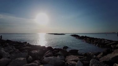 Sabah güneşi, İtalya 'nın Cesenatico kentindeki sakin Adriyatik Denizi üzerinde yükseliyor. Işık, güzel bir yaz sabahında kayalık bir dalgakırandan görülen sakin suyu yansıtır. Yüksek kalite 4k görüntü