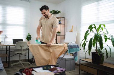 Genç işadamı iş gezisinden önce otel odasında gömleğini ütülüyor.