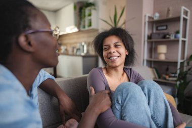 Mutlu genç çift birlikte eğleniyor, evdeki kanepede dinleniyor ve gülümsüyor.